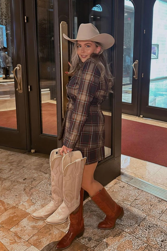 A women wearing a cowboy hat holding a pair of Justin Vintage boots.